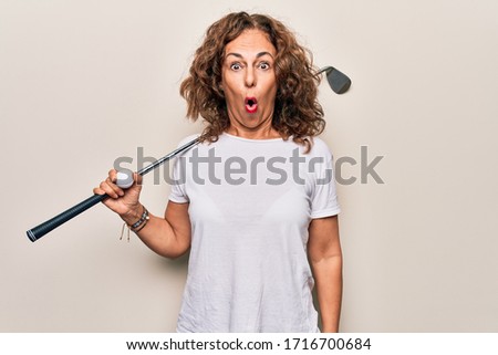 Middle age beautiful sportswoman playing golf using stick and ball over white background scared and amazed with open mouth for surprise, disbelief face