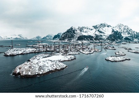 Drone aerial shots, photos in Henningsvaer, Lofoten Norway during cloudy weather winter time with snowy epic mountains, lot of islands and amazing light. Old fishing village with boats and ships. 