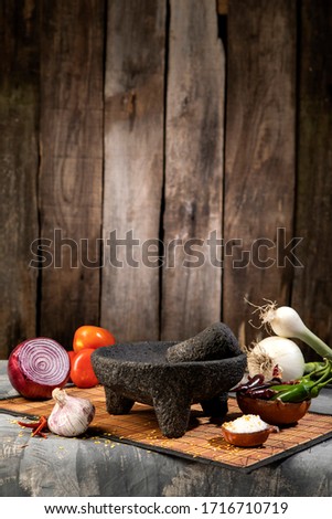 Traditional molcajete to make Mexican sauce with vegetables, on rustic wooden background. Salt, chili, garlic, onion, tomato.