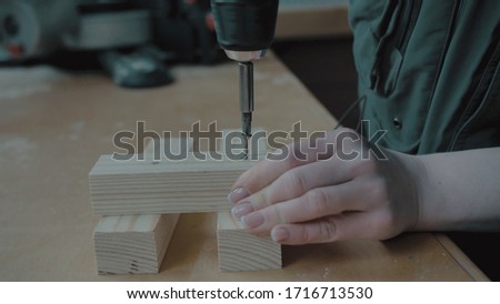 Girl with manicure twists a screwdriver into a wooden blank