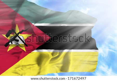 Mozambique waving flag against blue sky with sunrays