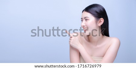 Beauty spa woman with perfect skin portrait. Beautiful asian spa girl smiling and showing empty copy space on index finger for text. Proposing product. Gestures for advertisement. Blue background