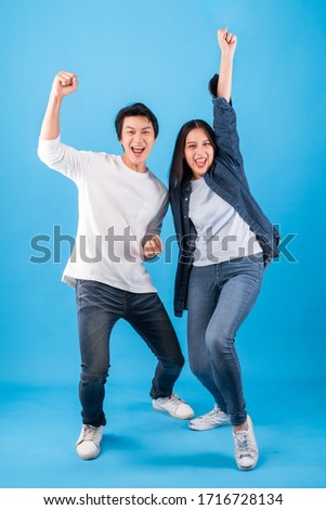 Excited young Asian couple man and woman happy celebrate success over blue background, winner concept