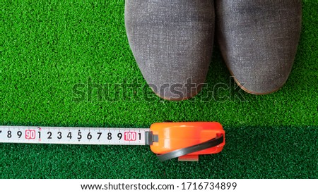 The tip of a pair of gray shoes with a measuring tape in front, showing the measurement at 1 meter, hinting the social distancing requirement of at least 1 meter apart amidst the COVID-19 pandemic. Royalty-Free Stock Photo #1716734899