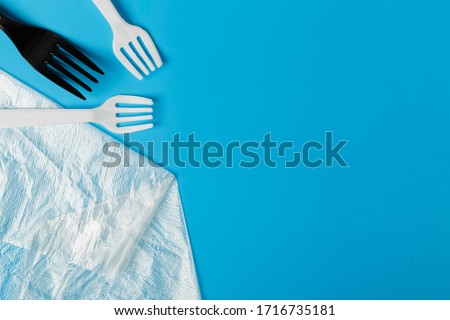  White and black plastic forks and transparent plastic bag on a blue background. The global problem of environmental pollution. Copy space. flat lay minimalism 