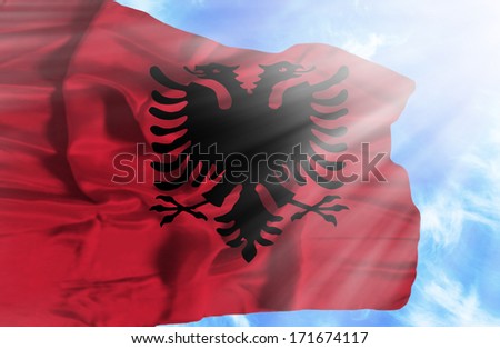 Albania waving flag against blue sky with sunrays