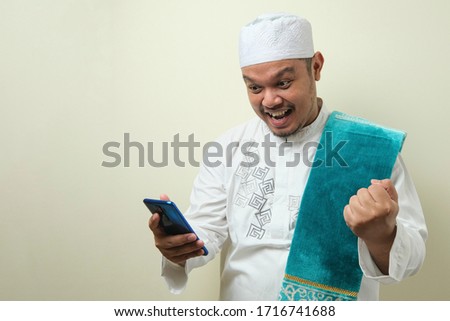 Fat Asian Muslim men looks surprised at the good news he received from his smartphone. Men show shocked gestures with glaring eyes at a smartphone. blue background