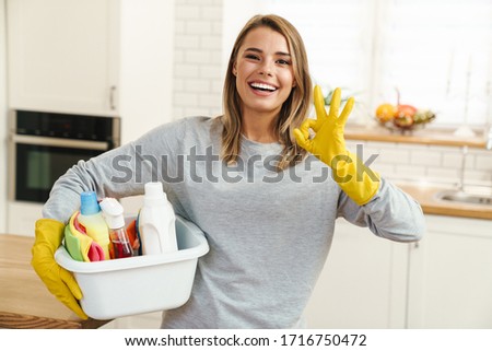 Photo of smiling young woman housewife in gloves holding cleanser bottles and showing ok sign at modern kitchen Royalty-Free Stock Photo #1716750472