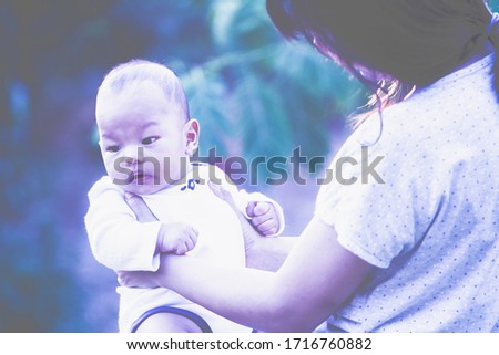 Cute baby in her mother arms outdoors portrait. asian having fun with little son, holding up male infant with arms mom standing beside at outdoor public park,  Mother's Day concept