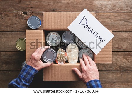 a person packing a donation box with food items Royalty-Free Stock Photo #1716786004