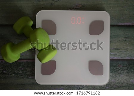 Weighing scales and green dumbbells on green wooden background. Top view. Sport flat lay