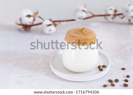Trendy korean iced dalgona coffee with cotton flower on the background, whipped instant coffee drink on pink marble table