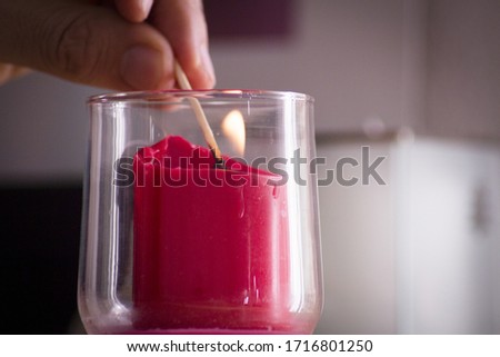Fingers of man lighting a red candle inside a transparent glass vase with a match