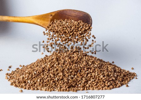 Buckwheat is poured from a wooden spoon onto a handful of buckwheat. Photo on a white background