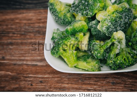 Frozen green cabbage, semi-finished product in a white cup. On a dark wood table. Cooking broccoli cabbage.