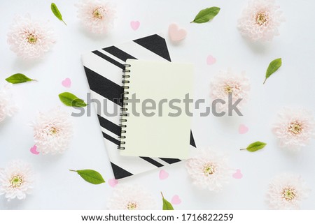 
yellow and black and white striped notebooks, we hold a heart and many pink flowers of chrysanthemums and green leaves on a white table.