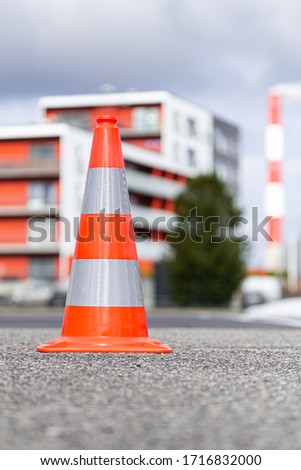 Orange gray white isolated traffic sign front left on asphalt matching background building chimney funnel stack right