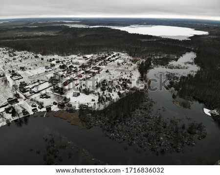 under village in the forest near big wide river with wooden bridge at winter with multiple lakes on backside. Aerial view