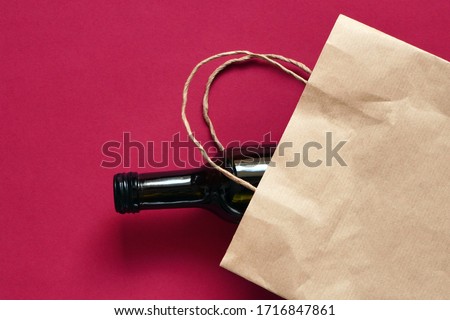 Paper bag with dark glass bottle of wine, alcohol present. Flat lay on maroon background, zero waste. Garbage recycling Royalty-Free Stock Photo #1716847861