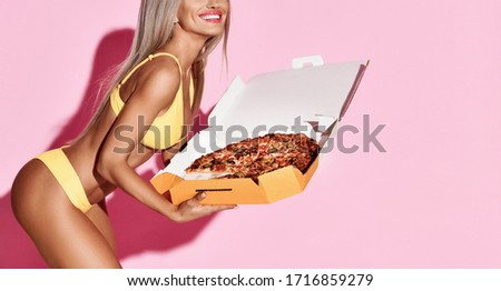 Beautiful slim blonde woman hold big pizza with pepperoni in delivery box happy smiling in yellow bikini on pastel color pink background