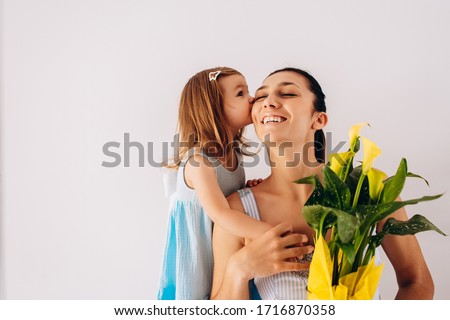 Caucasian little girl in blue dress is kissing her mom and giving her yellow flowers