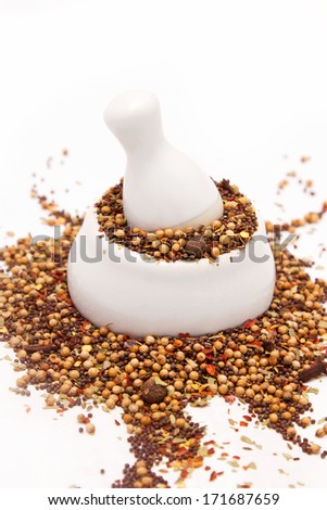 White porcelain mortar and pestle full of different spices and herbs; White background
