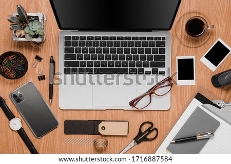 Office desk with laptop, cellphone and accessories in a woody background 