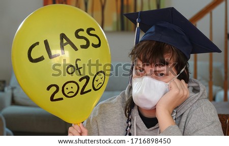 A graduating senior stuck at home in quarantine wears a mask and holds up a sad balloon - graduation for the class of 2020  is not what they had pictured.                              