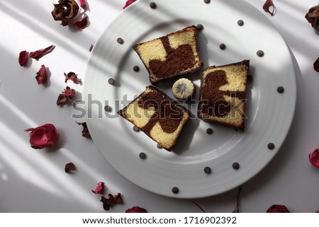 beautiful sweet food arrangement with marble cake, chocolate drops and dried, red rose petals on white background.