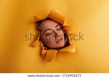 Pretty girl in hole of yellow background with watering can full of narcissus flowers. Creative photography.