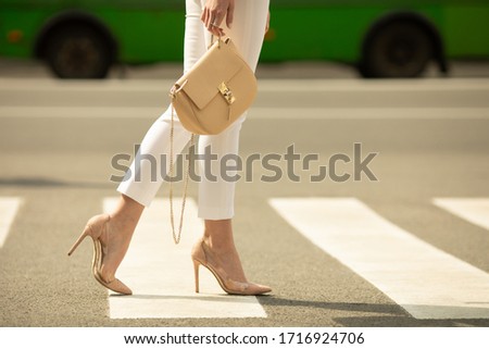 Сlose up of woman legs walking on crosswalk. The woman is wearing shoes on high heels. Handbag in woman hand.