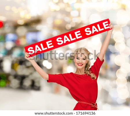 shopping, sale, christmas and mall concept - smiling woman in dress with red sale sign at shopping mall