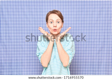 Portrait of surprised blond girl with white spots of cosmetic product on face skin, over shower curtain background. Care for imperfect, problem, acne prone skin. Skincare and beauty concept