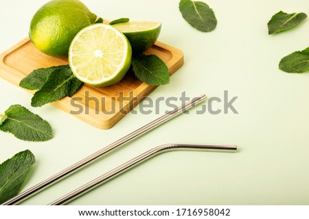 Reusable metal straws on a pastel background. Fresh lime and mint fruits lie on a wooden stand. Green color and fruts emphasize. Reusable environmental products, zero waste.Eco products Royalty-Free Stock Photo #1716958042