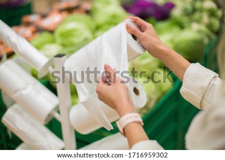 Adult woman taking one plastic package from the roll of packing plastic bags in the vegetable department of the supermarket or grocery store Royalty-Free Stock Photo #1716959302