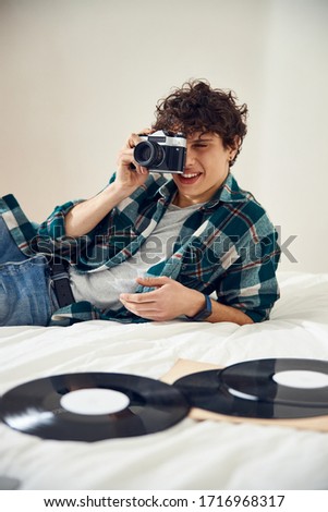 Handsome young man lying on bed with vinyl records and using retro camera stock photo