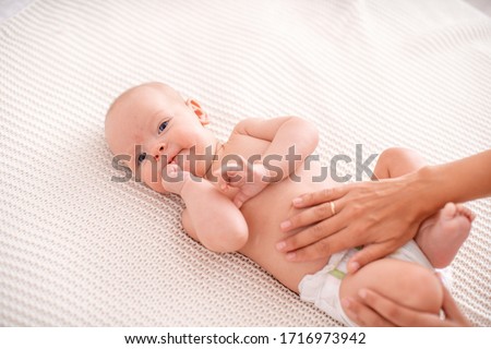 Baby massage. Masseur massaging tummy of baby during colic. Newborn colicky baby without clothes laying on her back, mother's hand on her tummy helping her with colic.