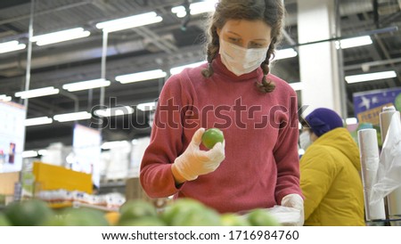 beautiful girl in rubber gloves and medical mask carefully selects lime for prevention diseases of covid-19 coronavirus, increasing immunity with vitamin C
