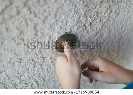 Boys hands ringing door bell outdoors on stucco wall.