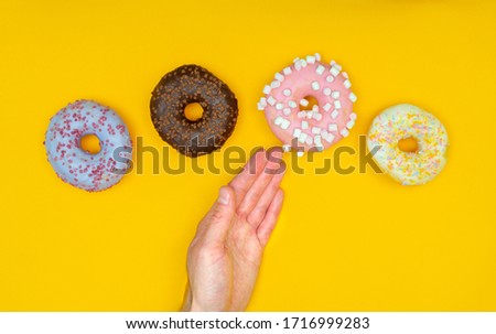 Sweet chocolate donut on yellow background and male hand. Dessert food