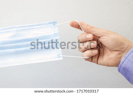 First person view of a man holding face mask on grey background. Protective raspiratory mask for spreading virus. Close up, copy space, top view, flat lay.
