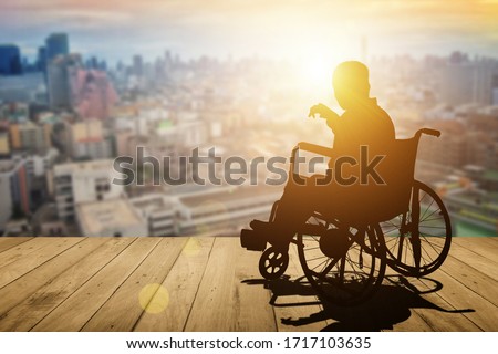Disabled person silhouette with hand lift on wheelchair have sunset city background. International Disability Day or Handicapped sport or Paralympics. Challenge and Conquer success and health concept.