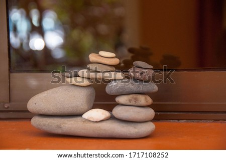 A lot of tiny stones are balanced in a difficult and challenging way. There is a shell between the stones. Reflecting on a window behind it.