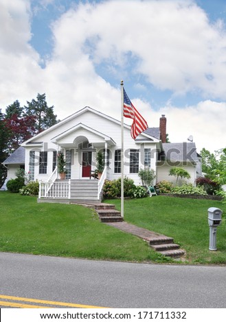 American Flag pole suburban cottage style home residential neighborhood USA blue sky clouds