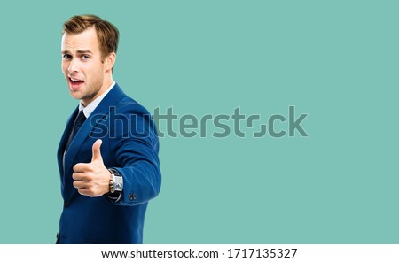 Excited businessman showing thumbs up like hand sign gesture, in green maine confident suit, over green color background. Handsome happy man. Copy space for some slogan or advertising text.