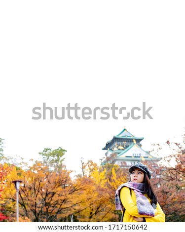 Asian tourist in yellow shirt and hat travel in autumn leaves tree park with osaka castle background sign seeing in Japan dream trip for leisure and explore. Abroad travel concept. Space for text.