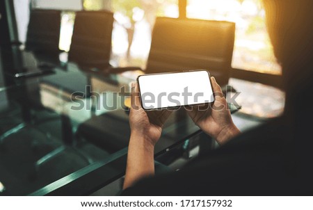 Mockup image of a woman holding mobile phone with blank white screen in office