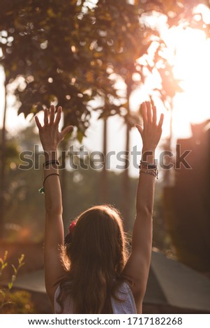 Woman holding hands in the air with orange sunlight in the background.