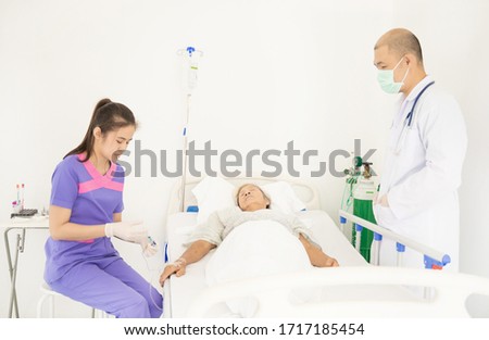Doctor, nurse and elderly woman patient in  bed at ward in hospital.