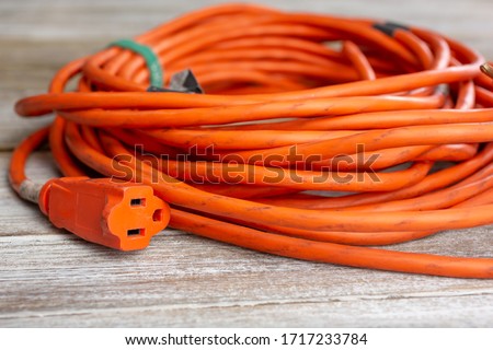 A view of an orange extension cord, featuring the female plug end, seen on a wooden surface. Royalty-Free Stock Photo #1717233784